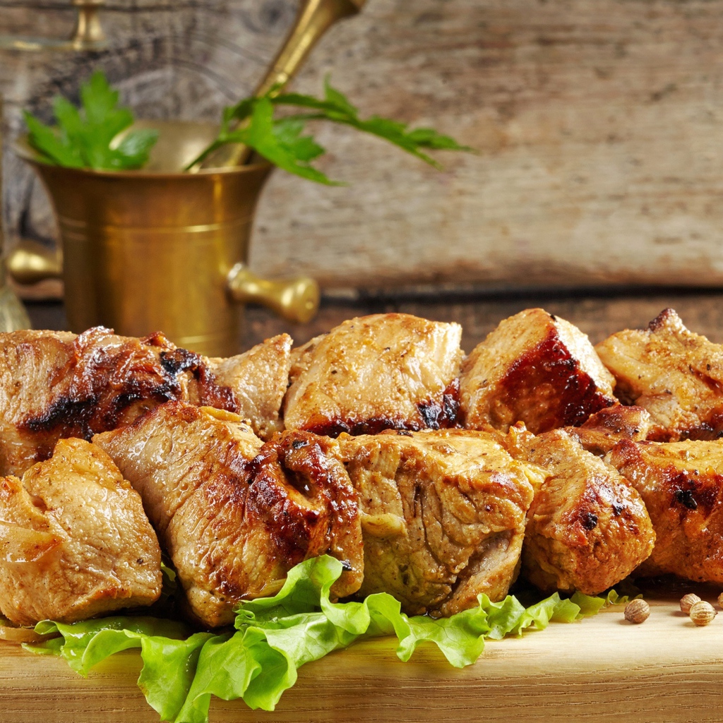 Аппетитный шашлык лежит на разделочной доске с листьями салата