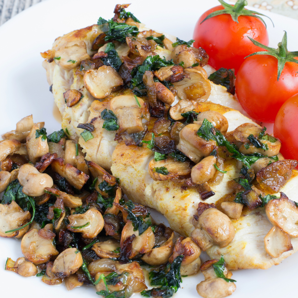 Аппетитный кусок куриного филе с грибами на тарелке с помидорами 