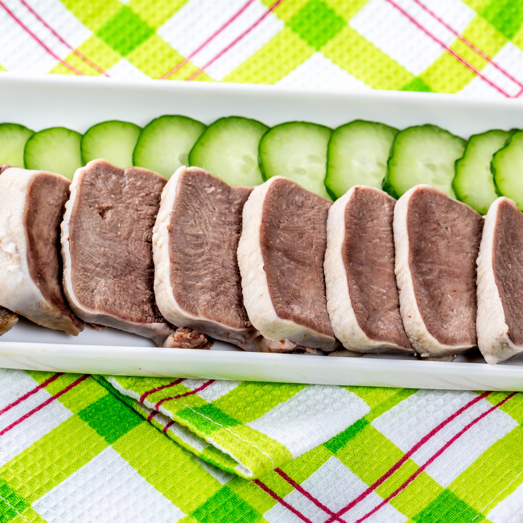 Вареный язык на тарелке со свежими огурцами