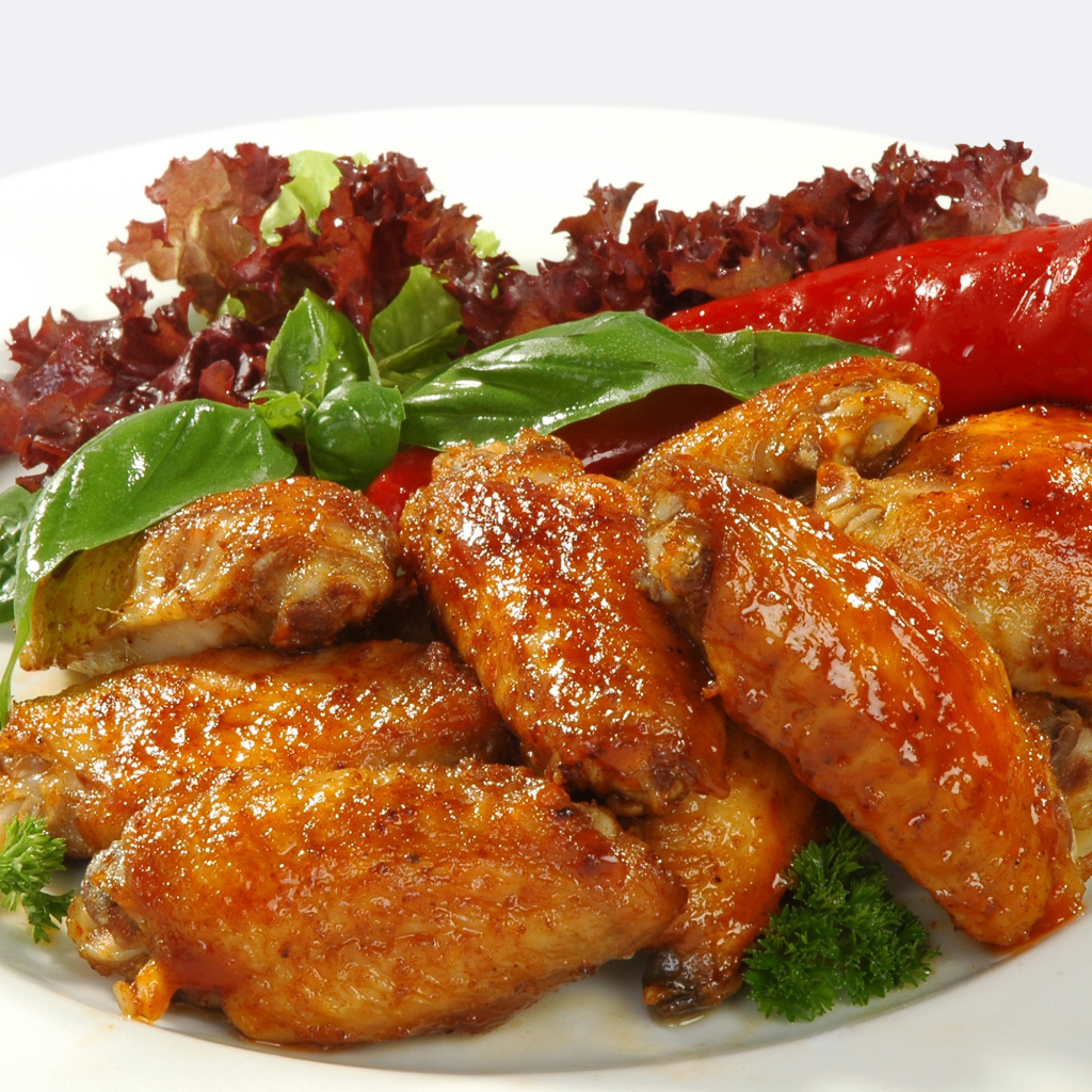 Жареные куриные крылышки на тарелке с острым перцем и зеленью 