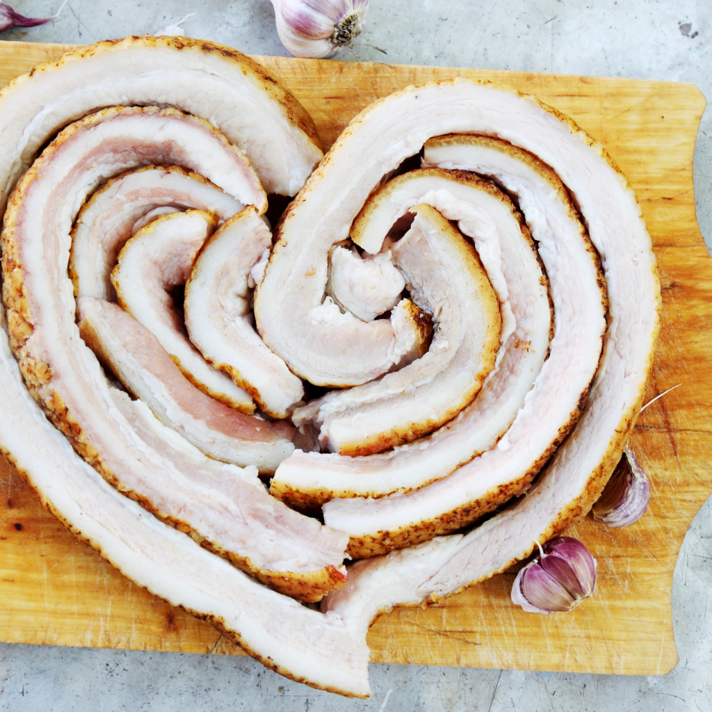 Сердце из свежего сала на доске с чесноком