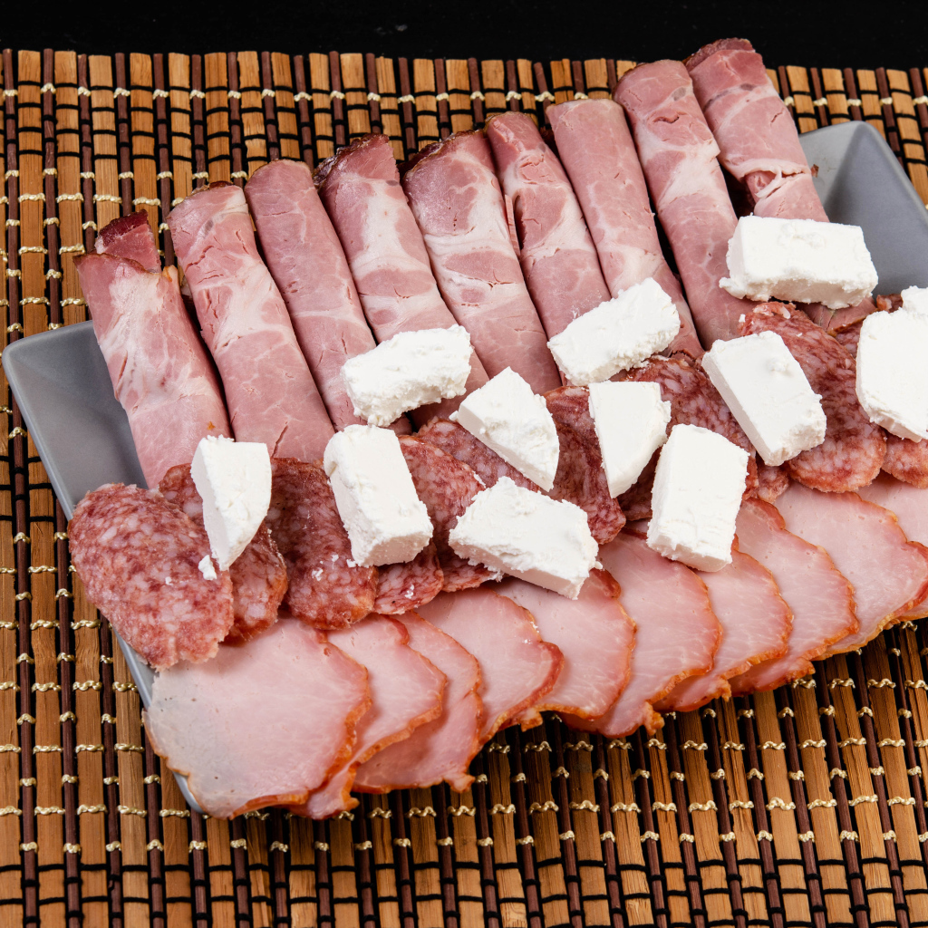 Колбаса и ветчина на тарелке с кусочками сыра фета