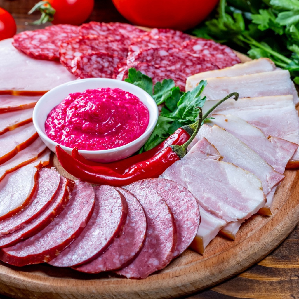 Мясная нарезка на доске с соусом, красным перцем,  помидорами и зеленью 