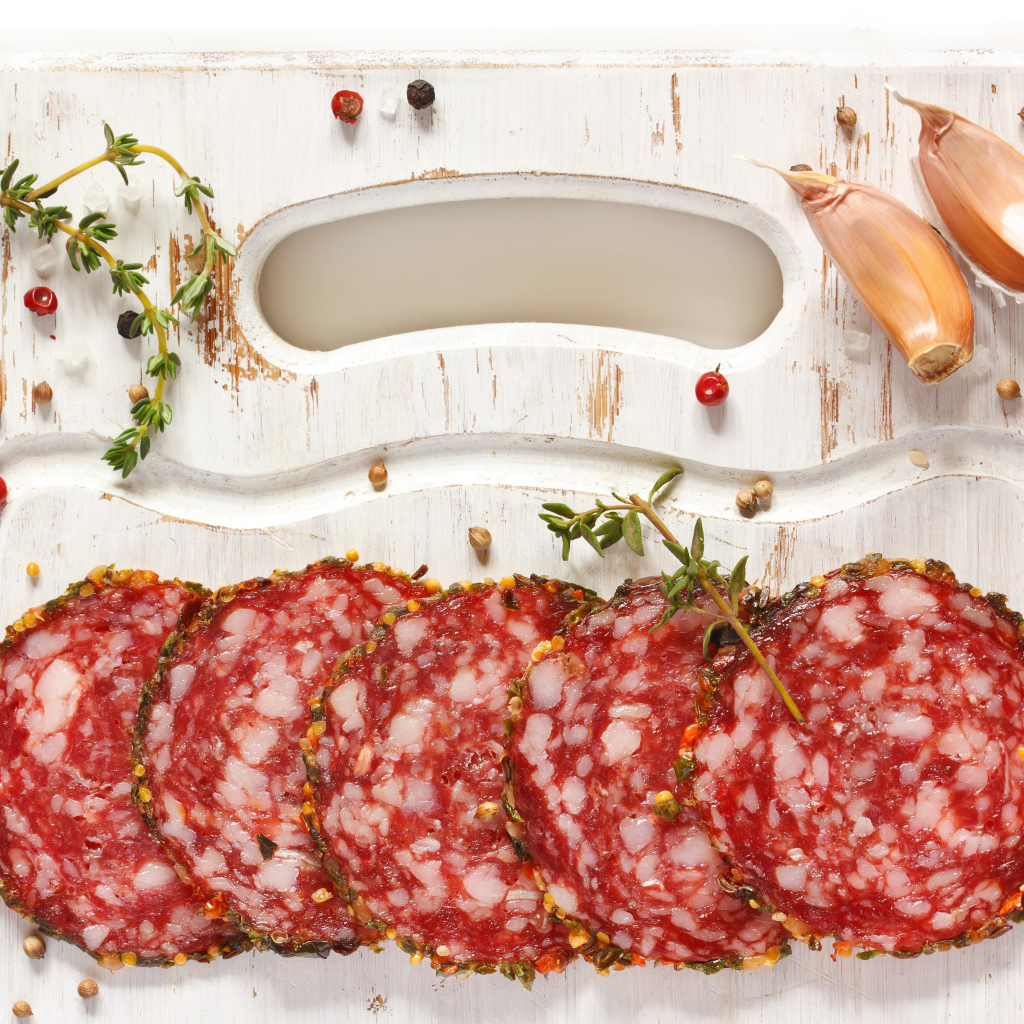 Нарезанная колбаса на разделочной доске со специями и чесноком