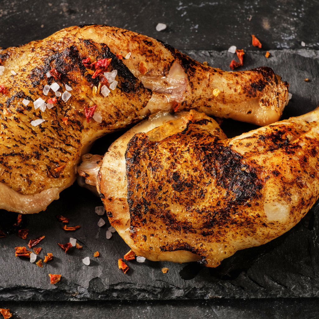 Два запеченных куриных окорочка на черном фоне