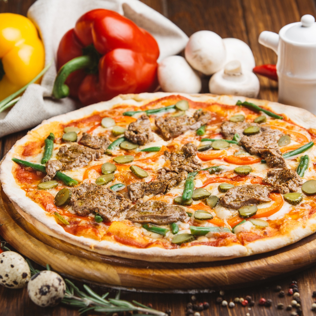 Свежая пицца с мясом и огурцами на столе с овощами