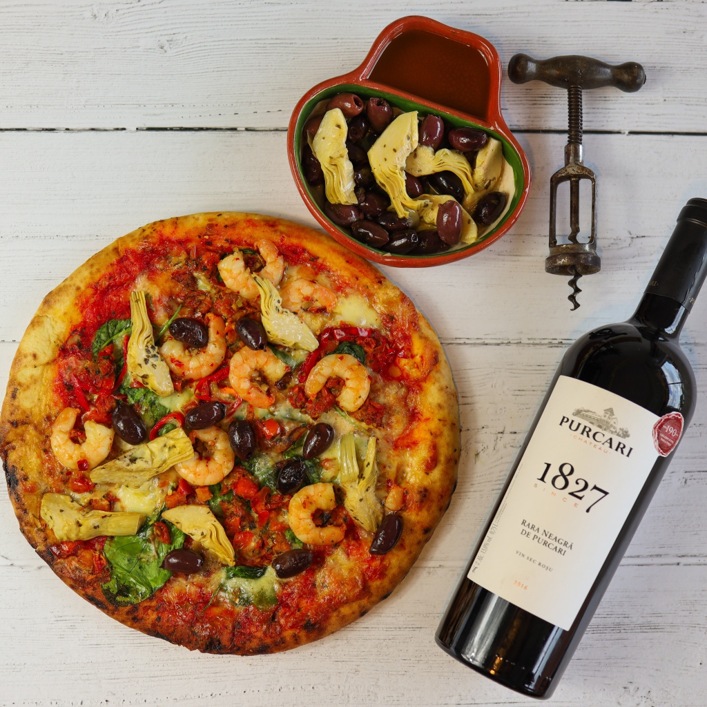 Пицца на столе с оливками и бутылкой вина