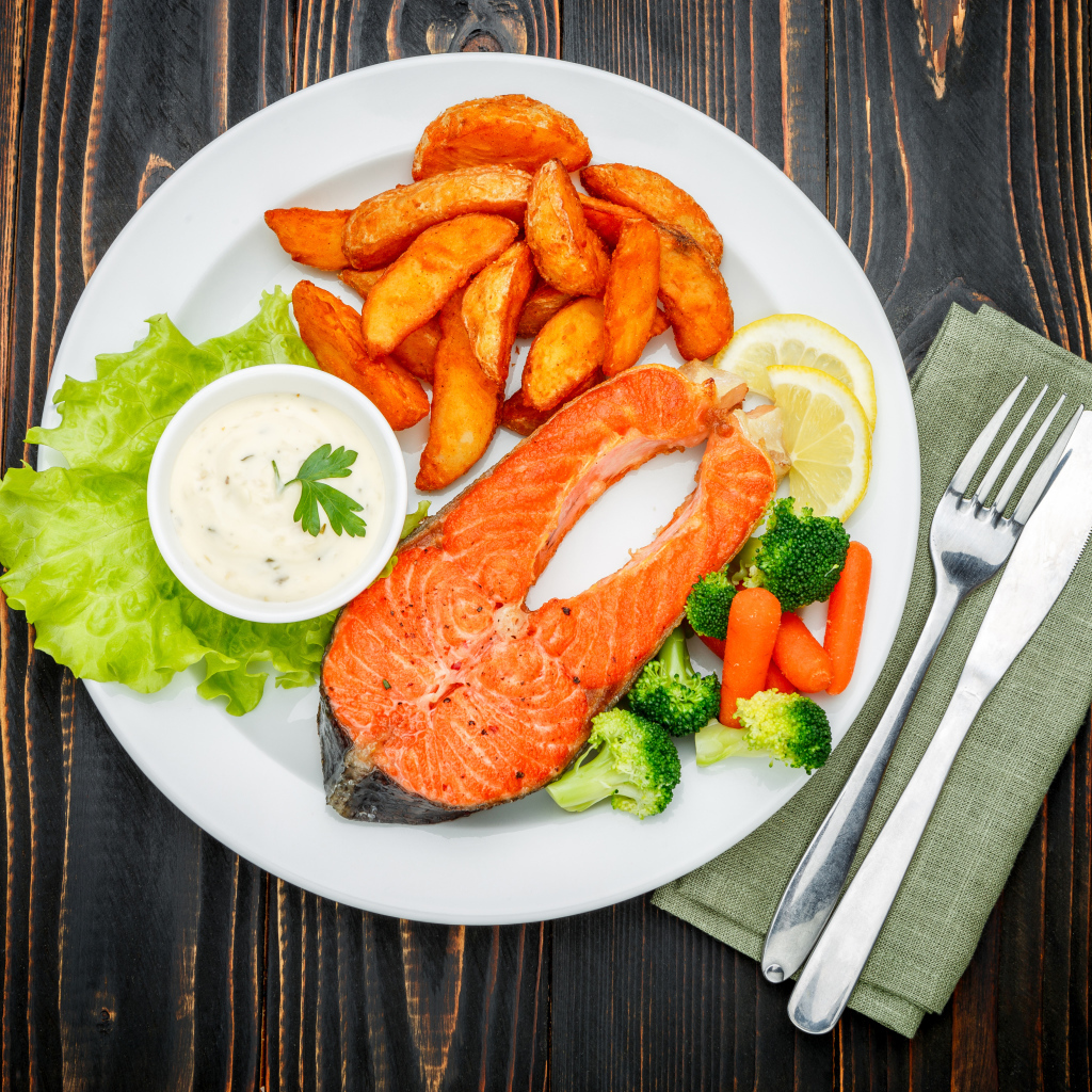 Кусок красной рыбы на тарелке с картофелем и соусом