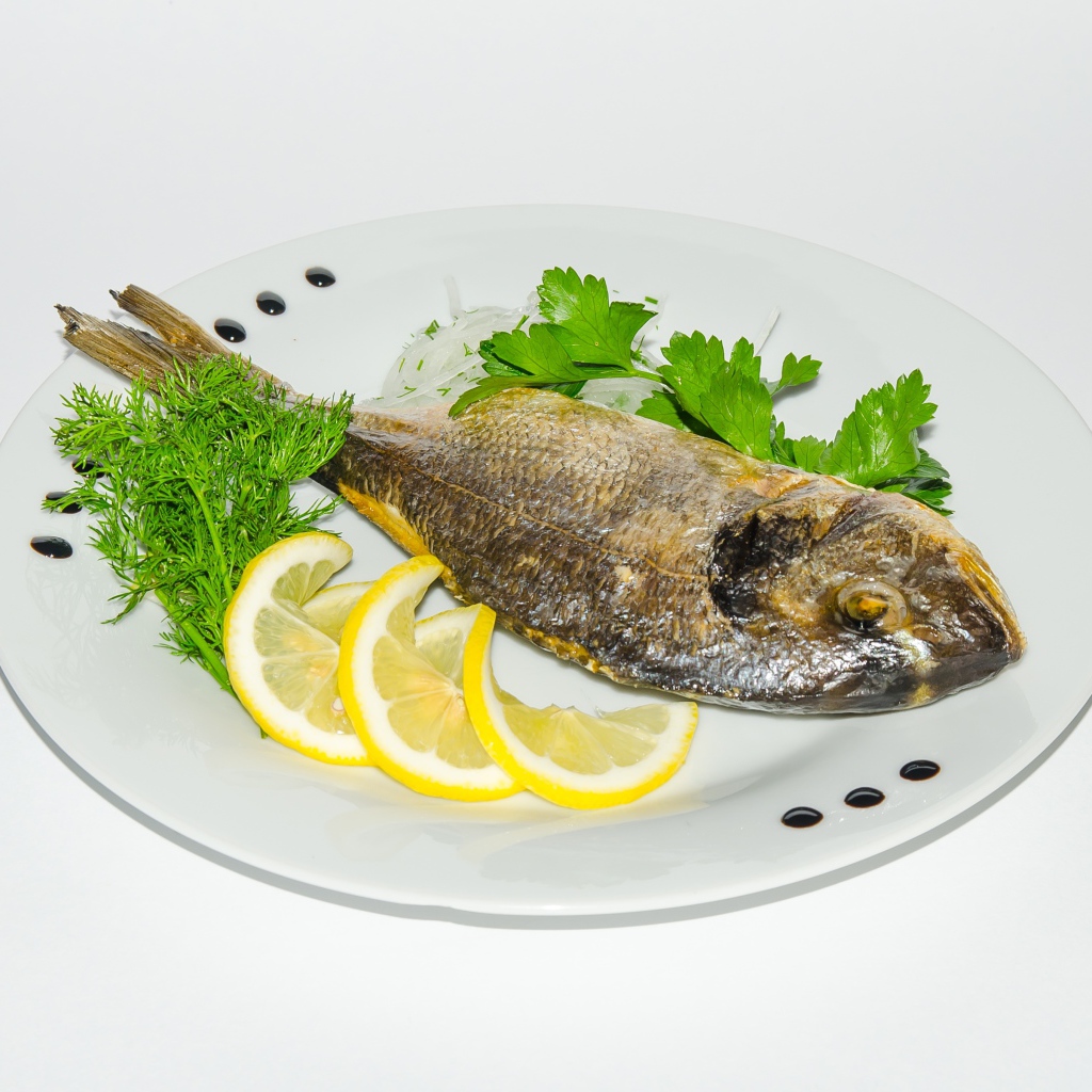 Запеченная рыба на тарелке с лимоном и зеленью 