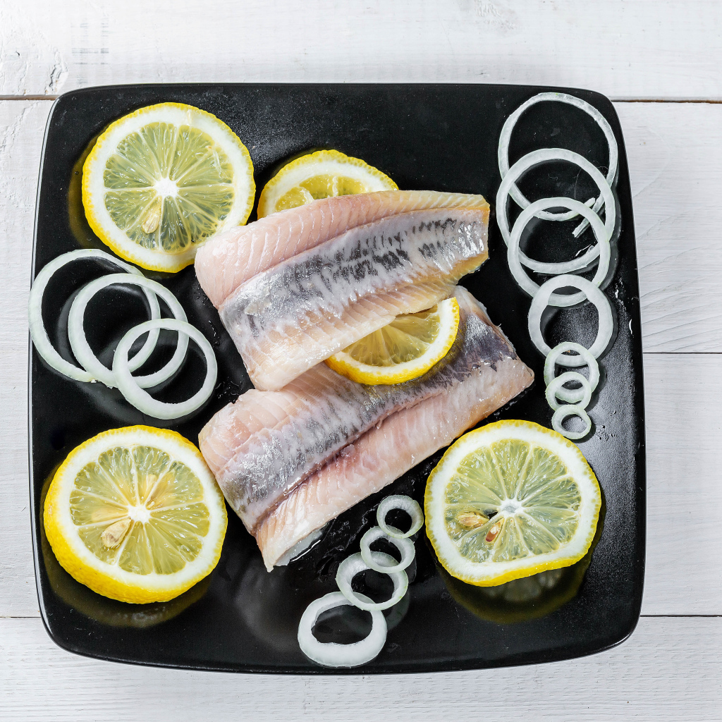 Филе сельди на черной тарелке с луком и лимоном