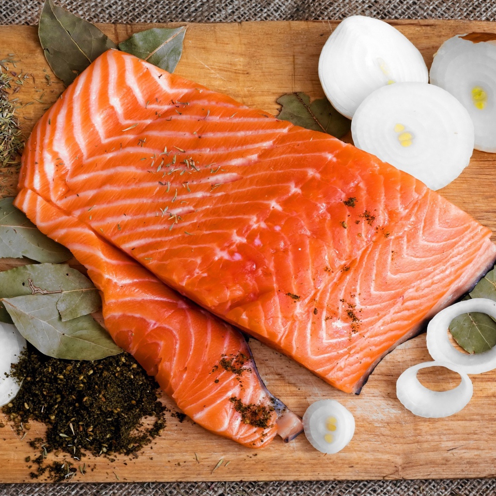 Куски красной рыбы на разделочной доске с луком и специями