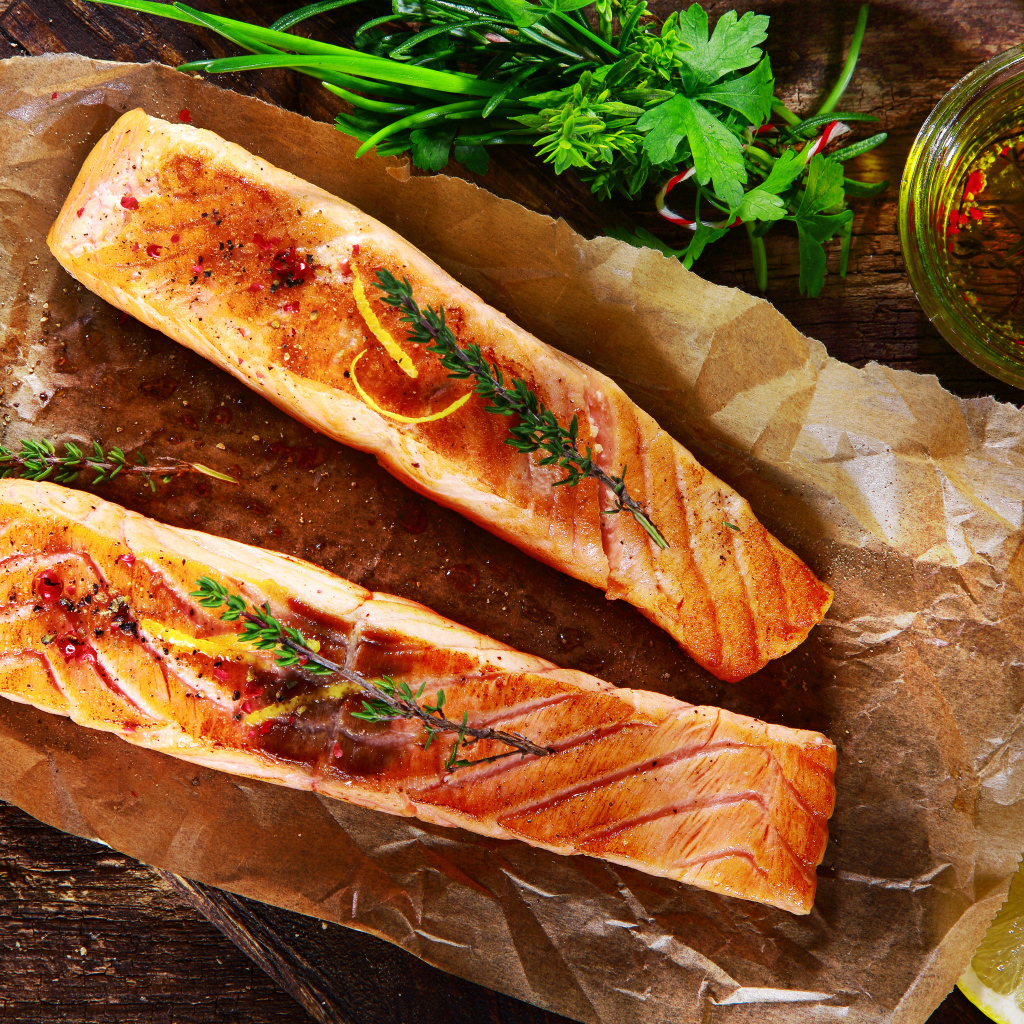 Два куска запеченной рыбы на столе с оливковым маслом и зеленью