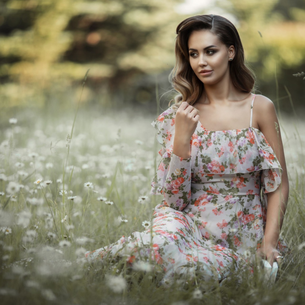 Красивая девушка в сарафане сидит на поляне с ромашками 