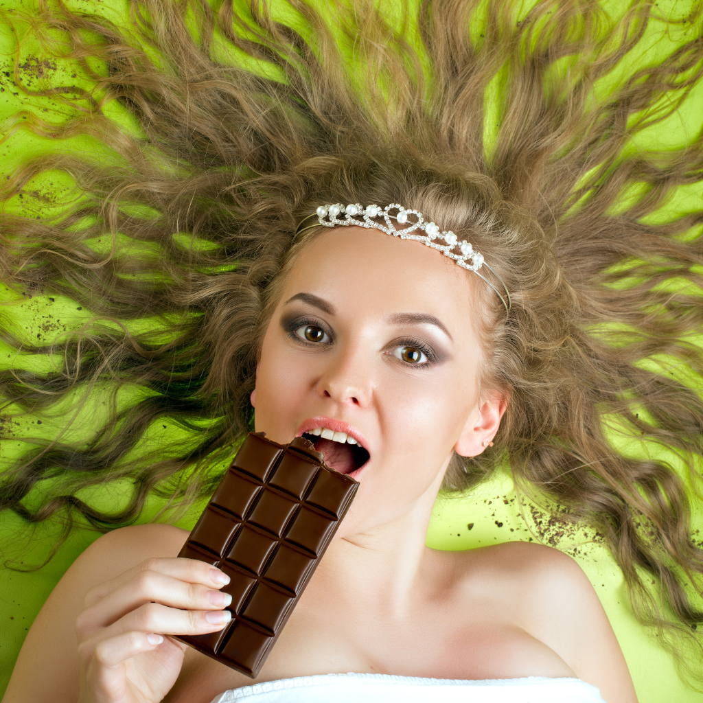 Красивая девушка с украшением в волосах лежит с шоколадкой 