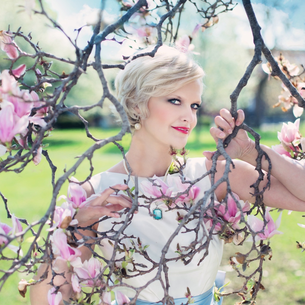 Красивая женщина с короткой стрижкой стоит у цветущей магнолии 