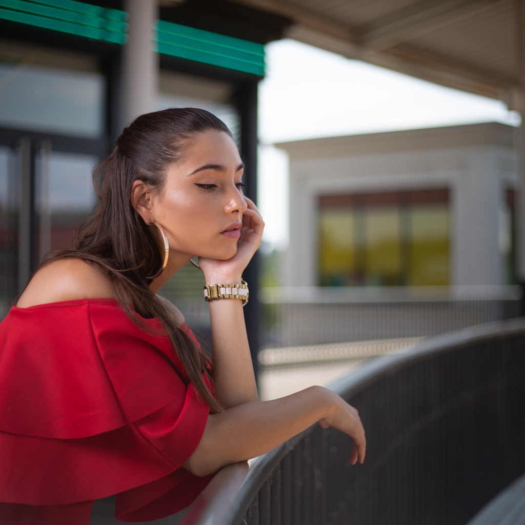 Задуманная девушка в красном платье стоит у перил 