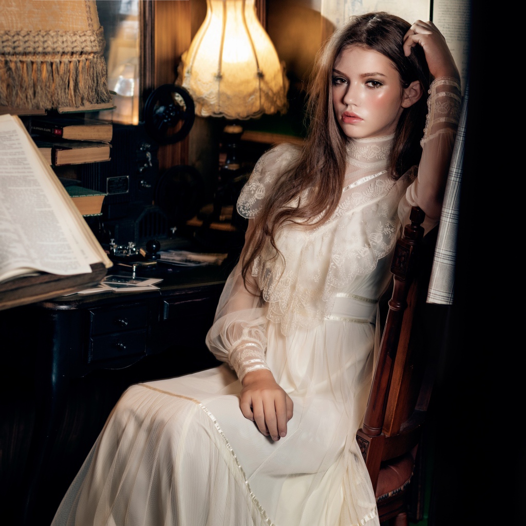 Девушка в красивом белом платье сидит на стуле у стола