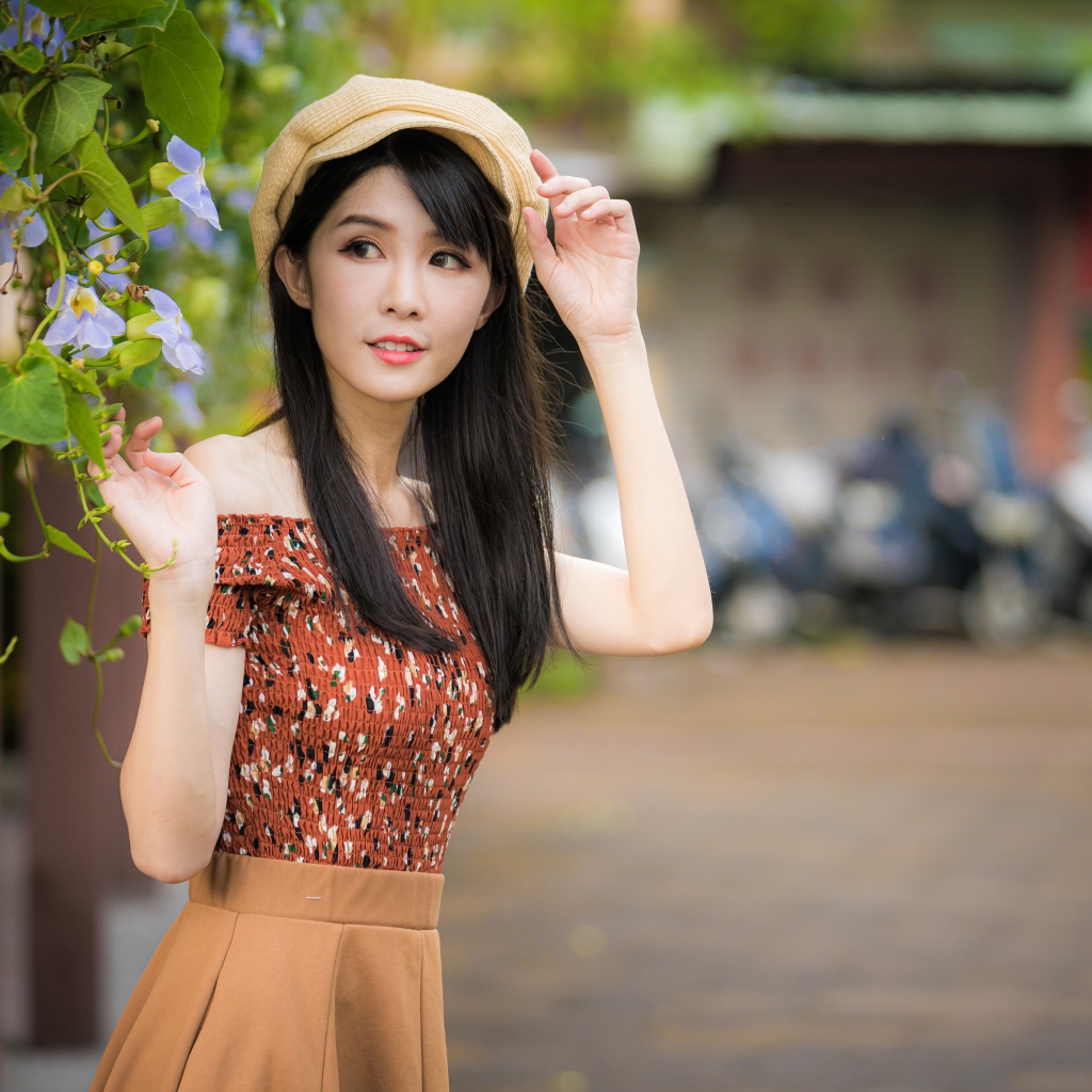 Молодая девушка азиатка в кепке стоит у голубых цветов