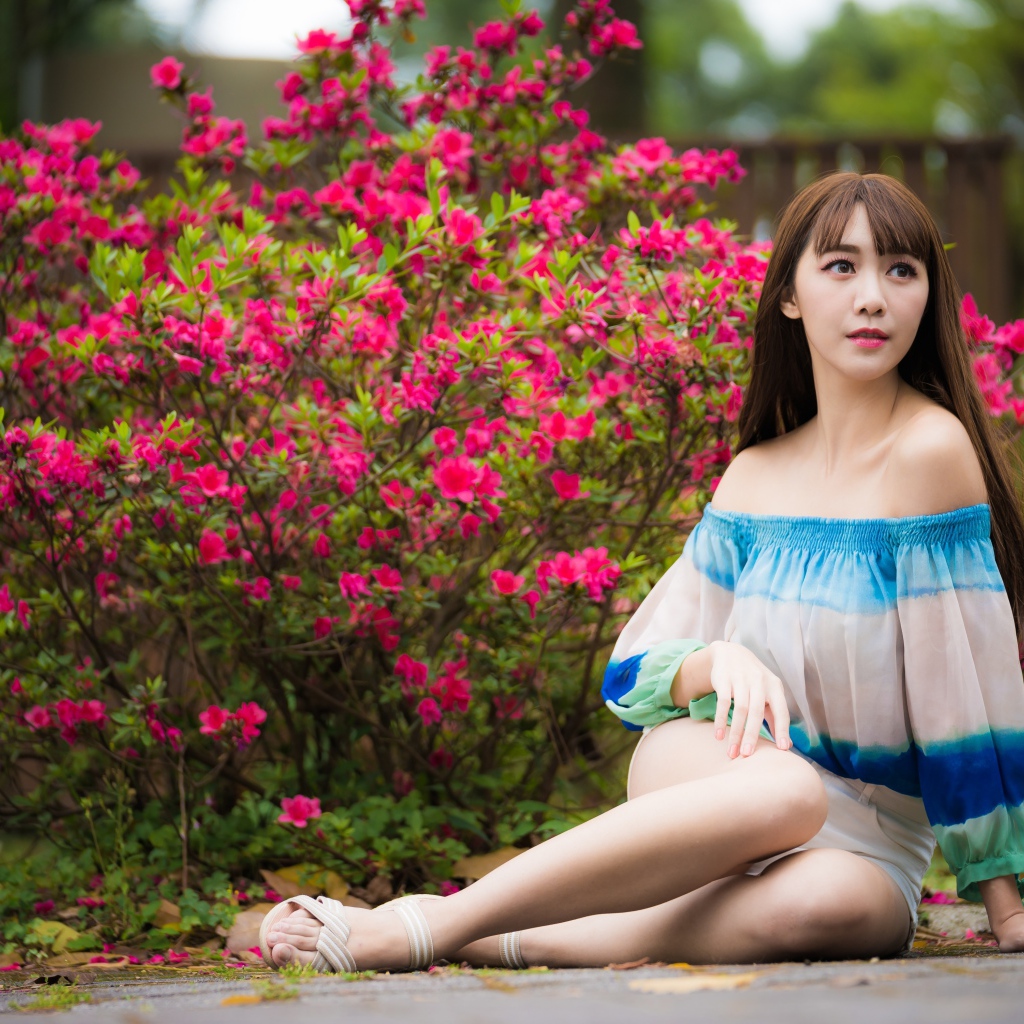 Молодая девушка азиатка сидит у куста с розовыми цветами