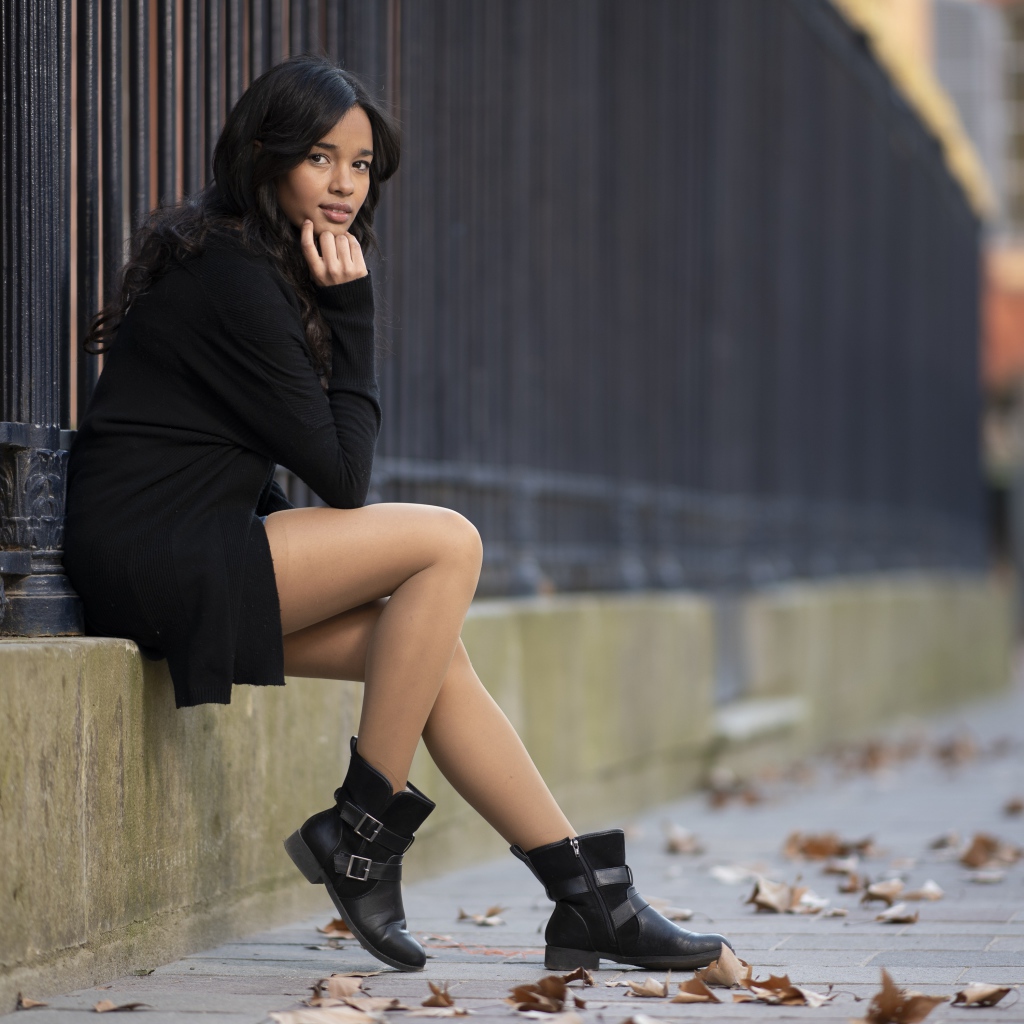 Молодая девушка в черном сидит у железного забора