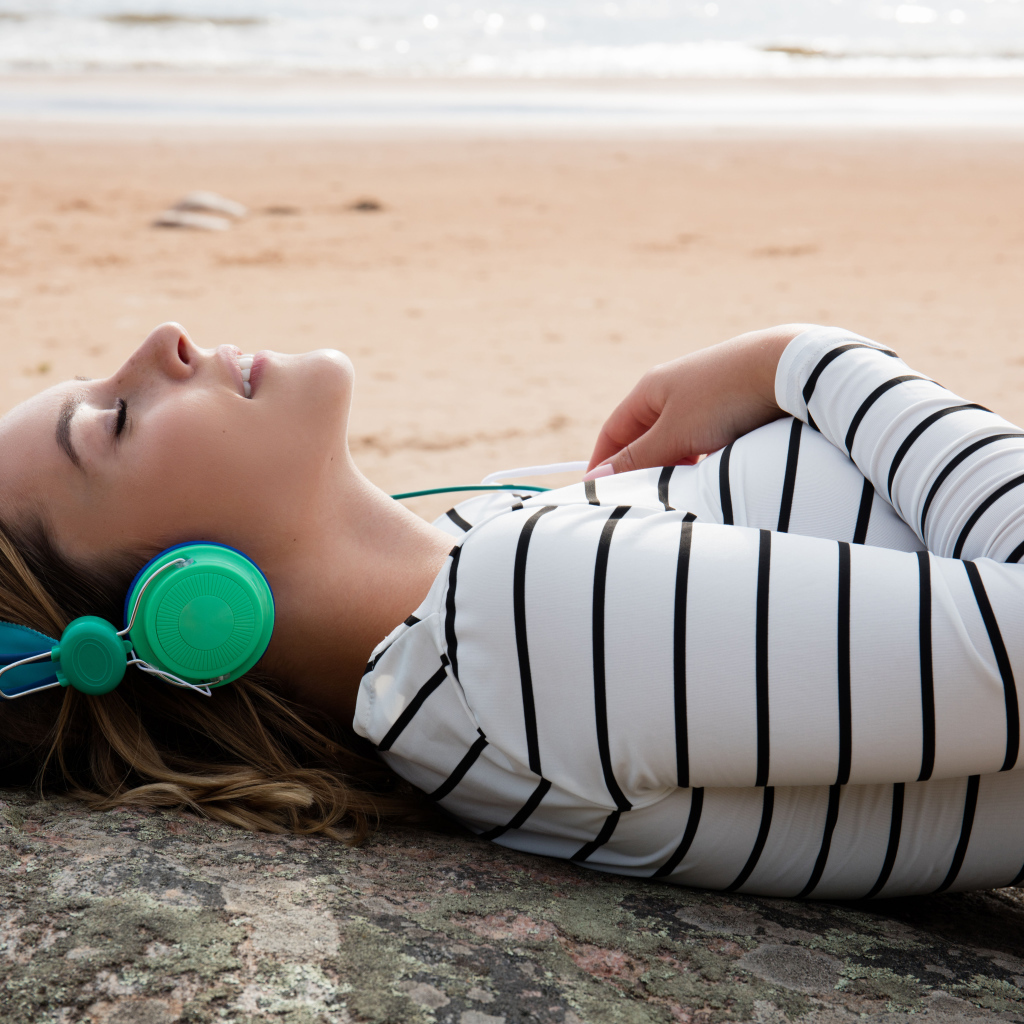 Молодая девушка лежит в наушниках на земле у моря