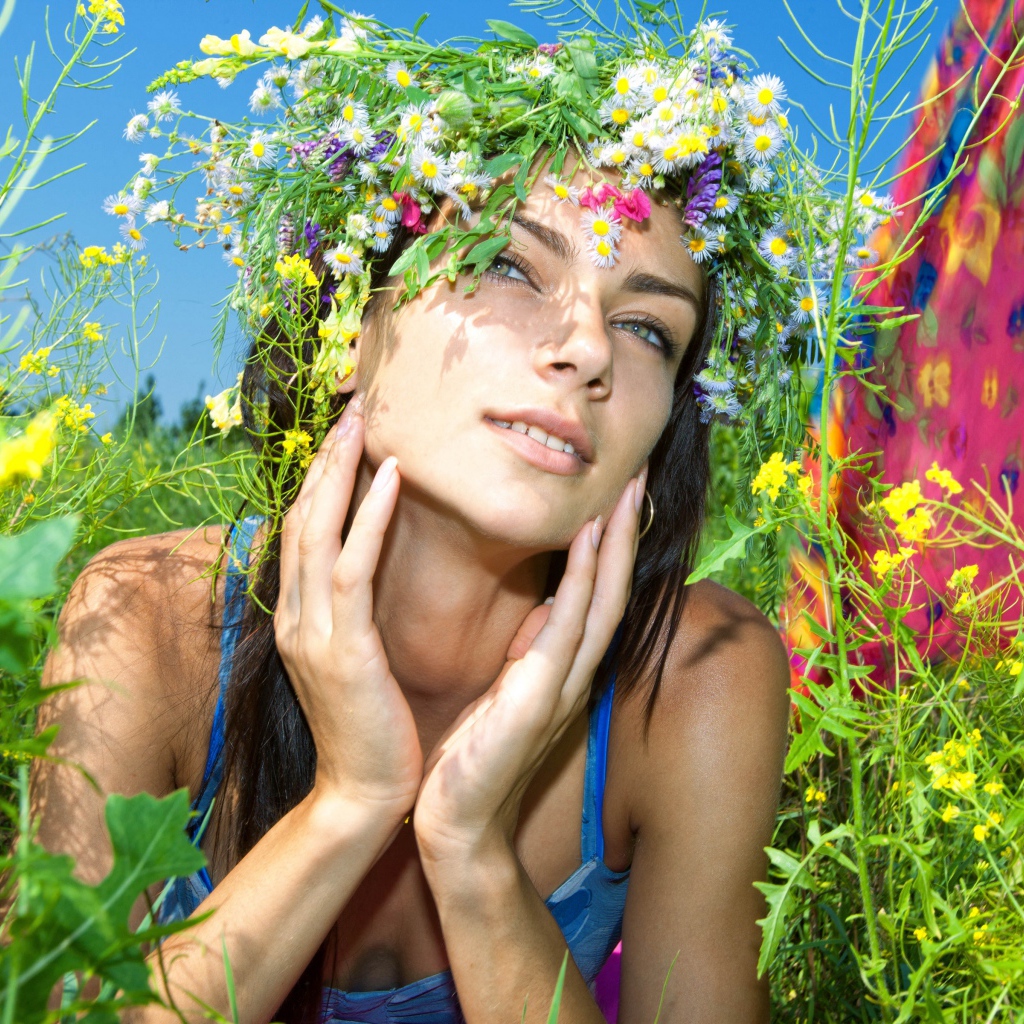 Молодая девушка с венком из полевых цветов лежит в траве