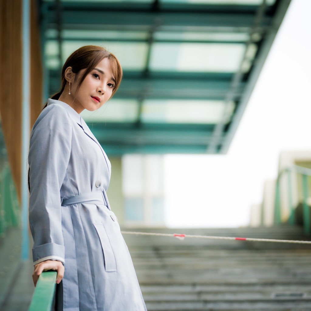 Девушка азиатка в пальто стоит у перил 