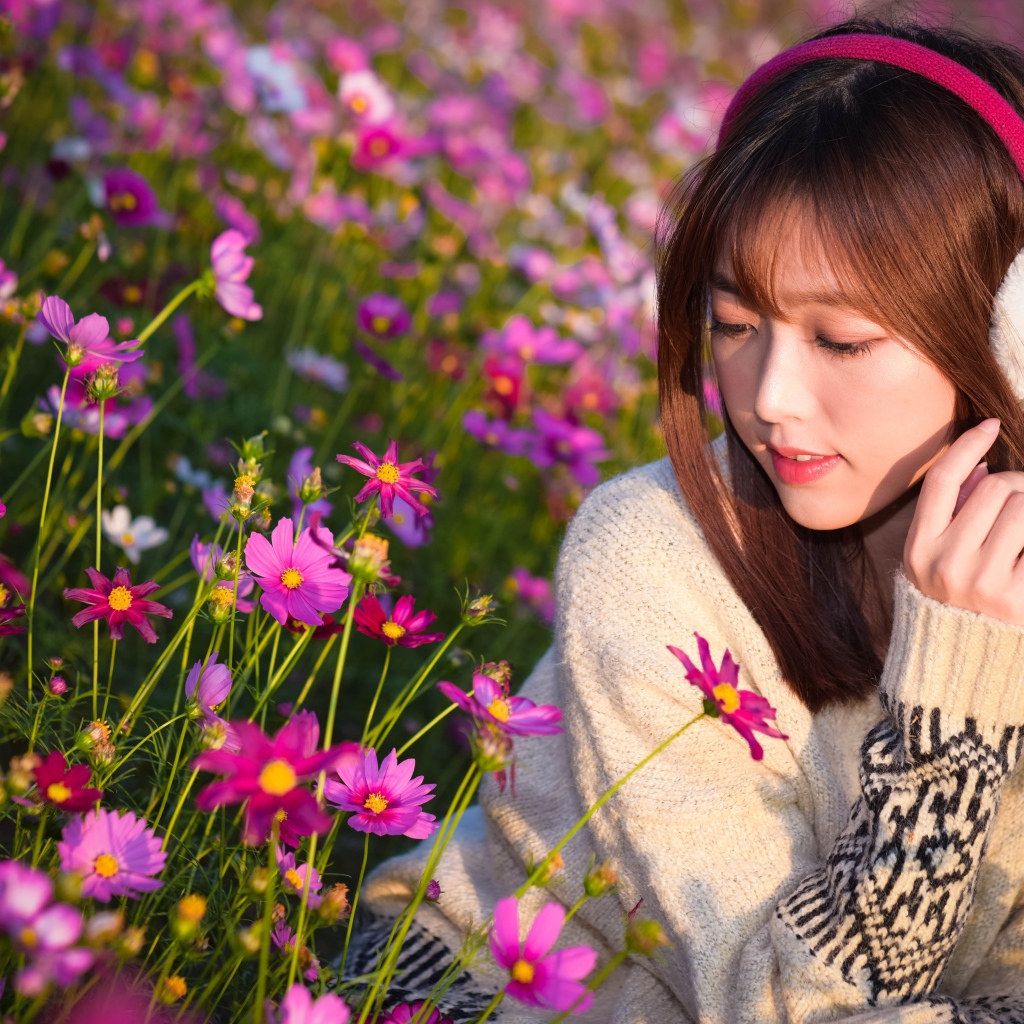 Девушка азиатка в наушниках сидит в цветах космеи