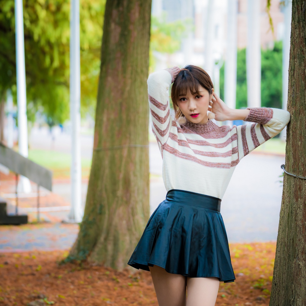 Девушка азиатка стоит в короткой юбке у дерева