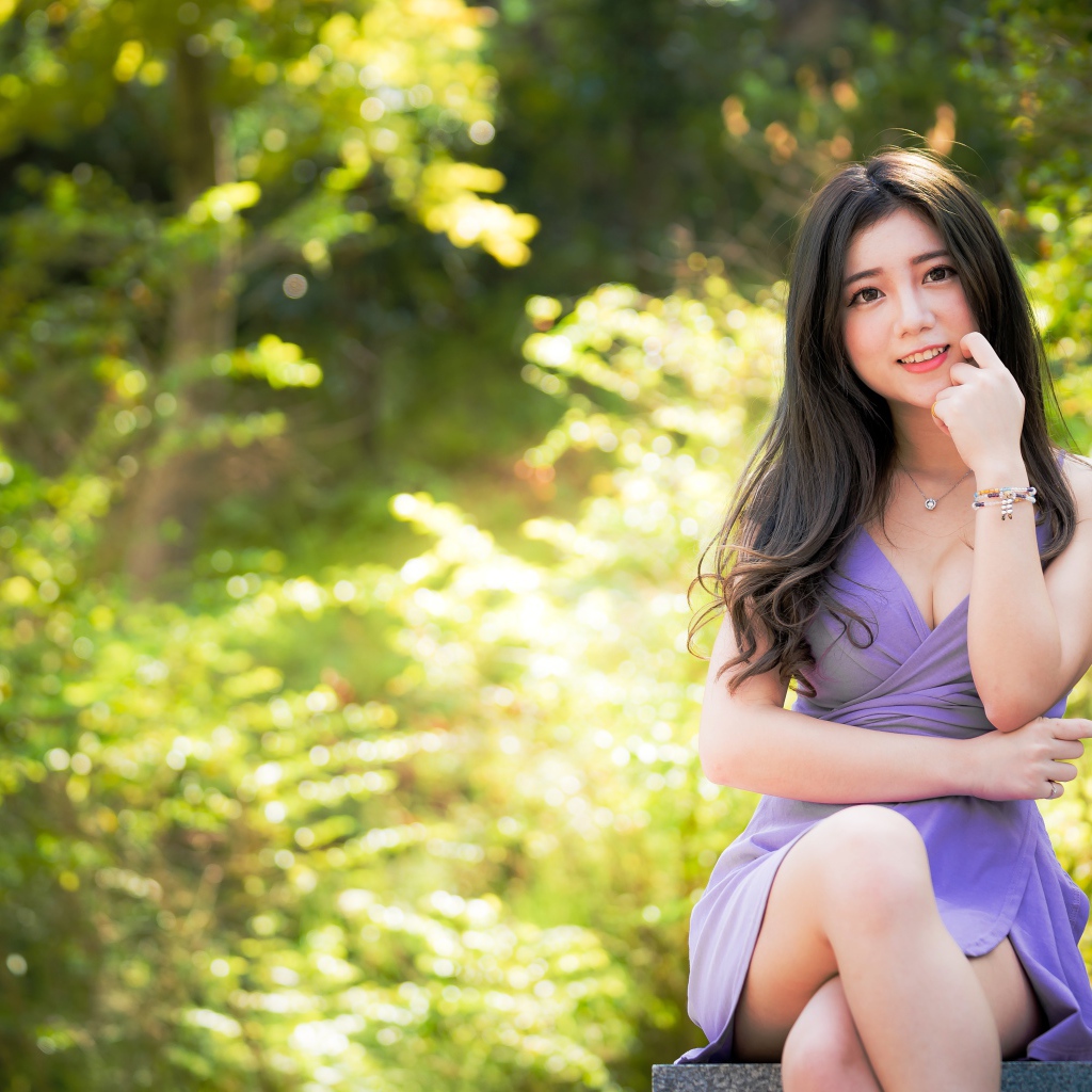 Молодая девушка азиатка сидит на лавке в парке