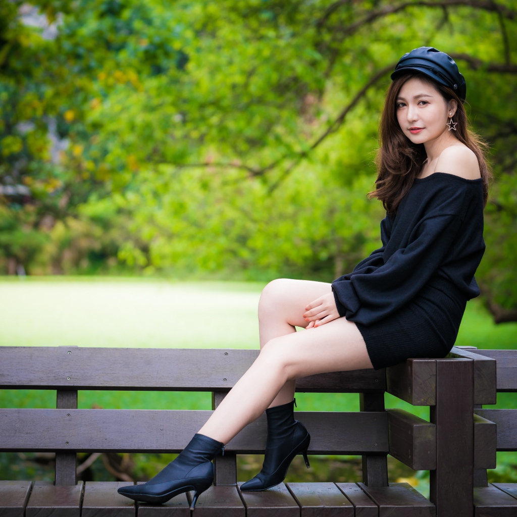 Красивая девушка азиатка в черном платье сидит на деревянной лавке