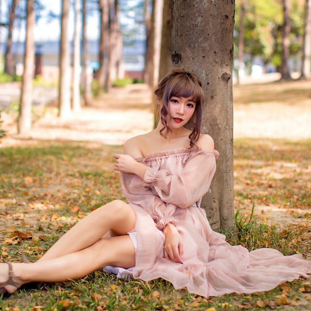 Красивая девушка азиатка в платье сидит под деревом