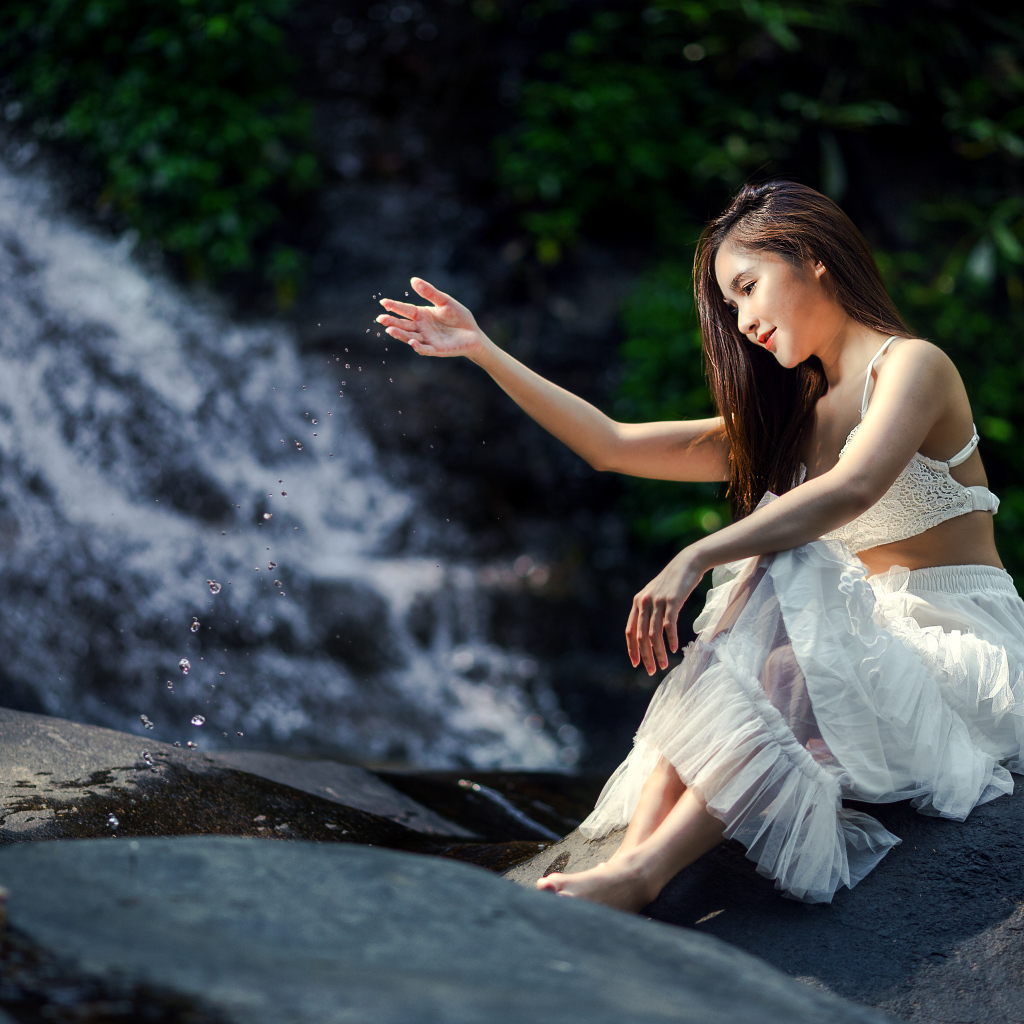 Красивая девушка азиатка в белом платье сидит у воды