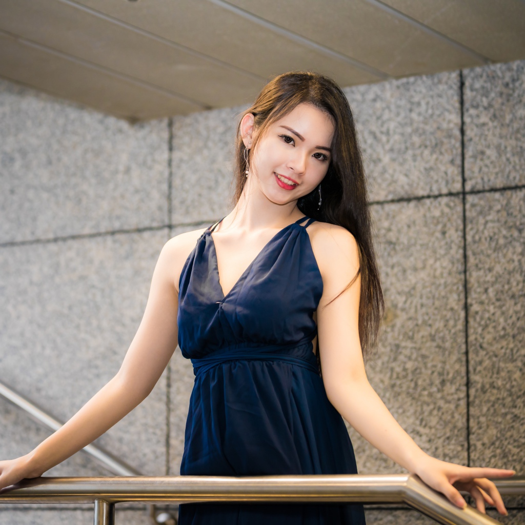 Красивая азиатка в черном платье стоит у перил