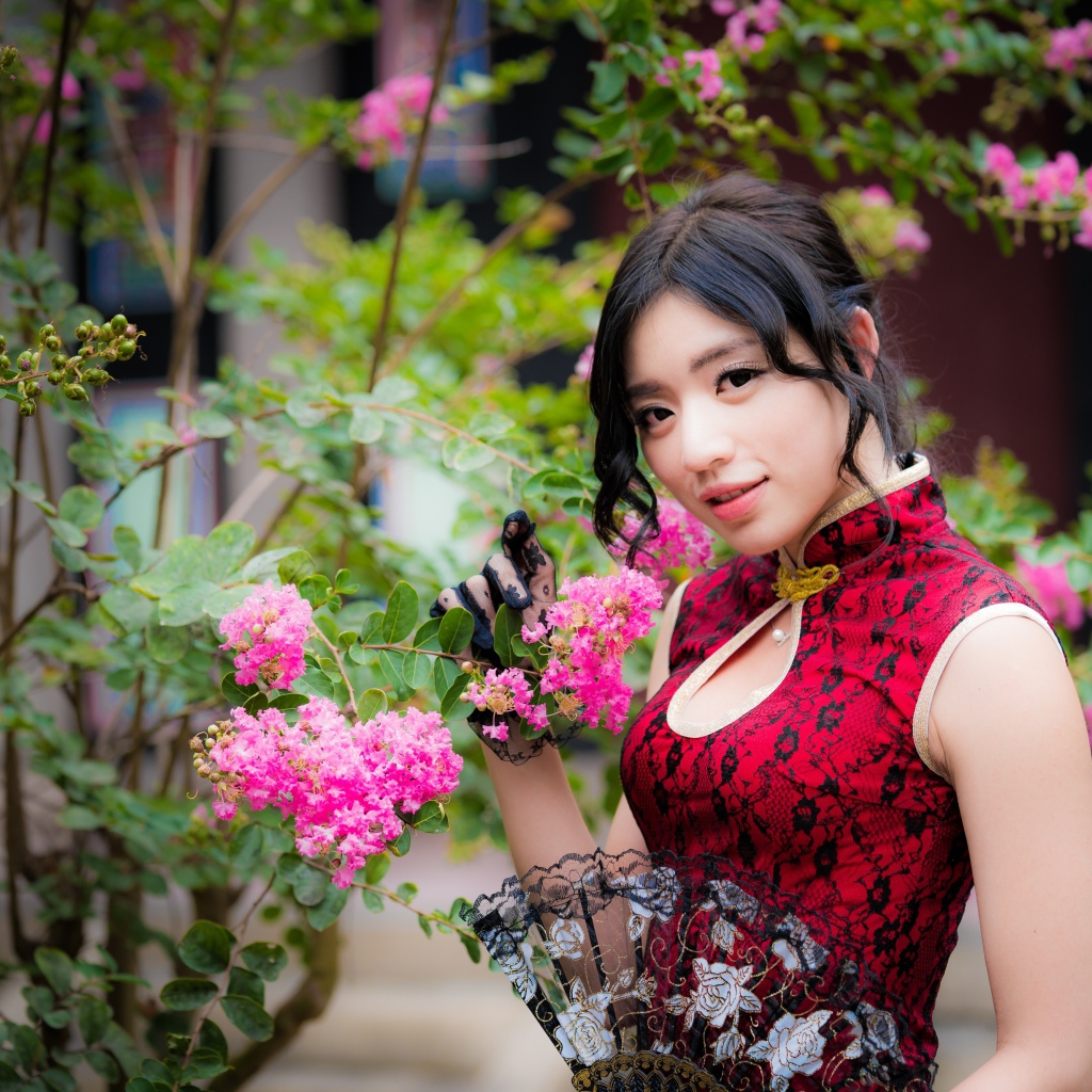 Красивая азиатка с веером в руках стоит у куста с розовыми цветами