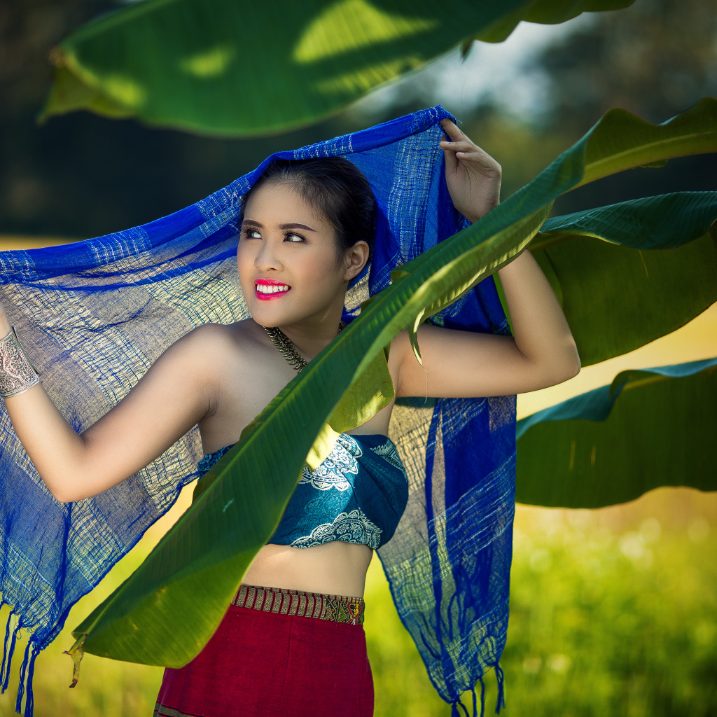 Красивая девушка азиатка с синим палантином у зеленых листьев