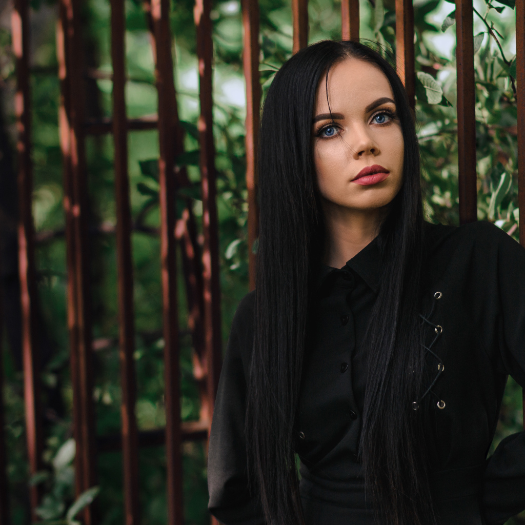 Красивая голубоглазая девушка в черном платье у железного забора