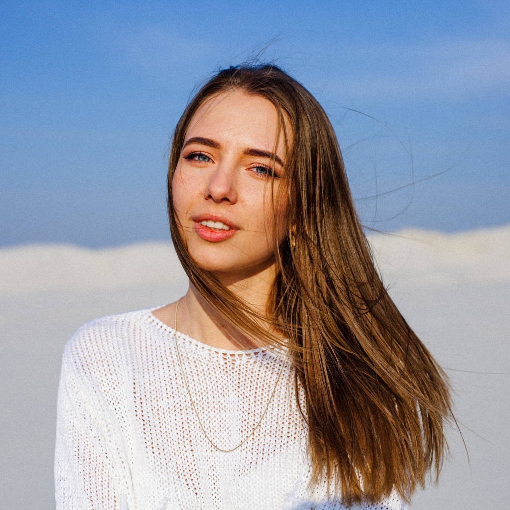 Красивая голубоглазая девушка в белом свитере на фоне голубого неба