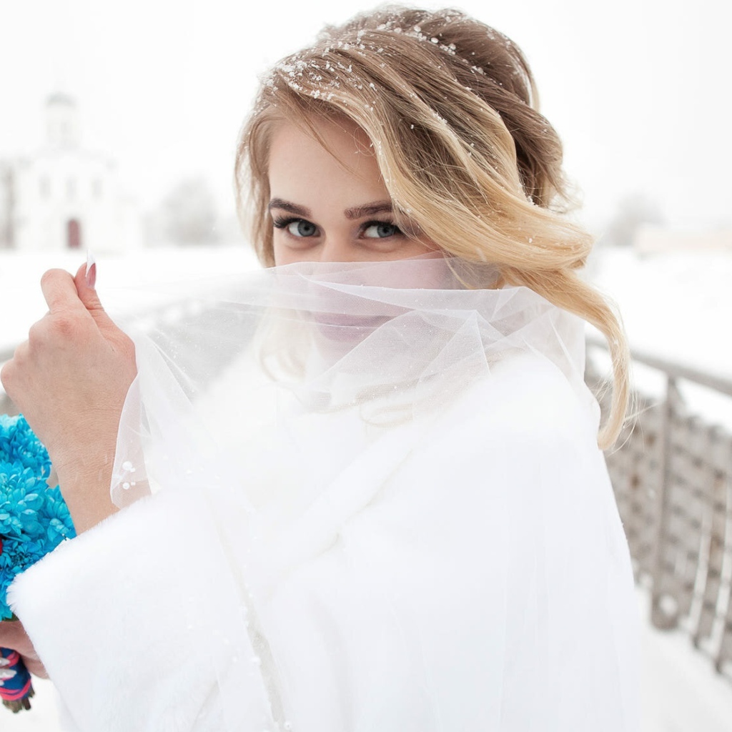 Красивая невеста с букетом в руках закрывает лицо фатой