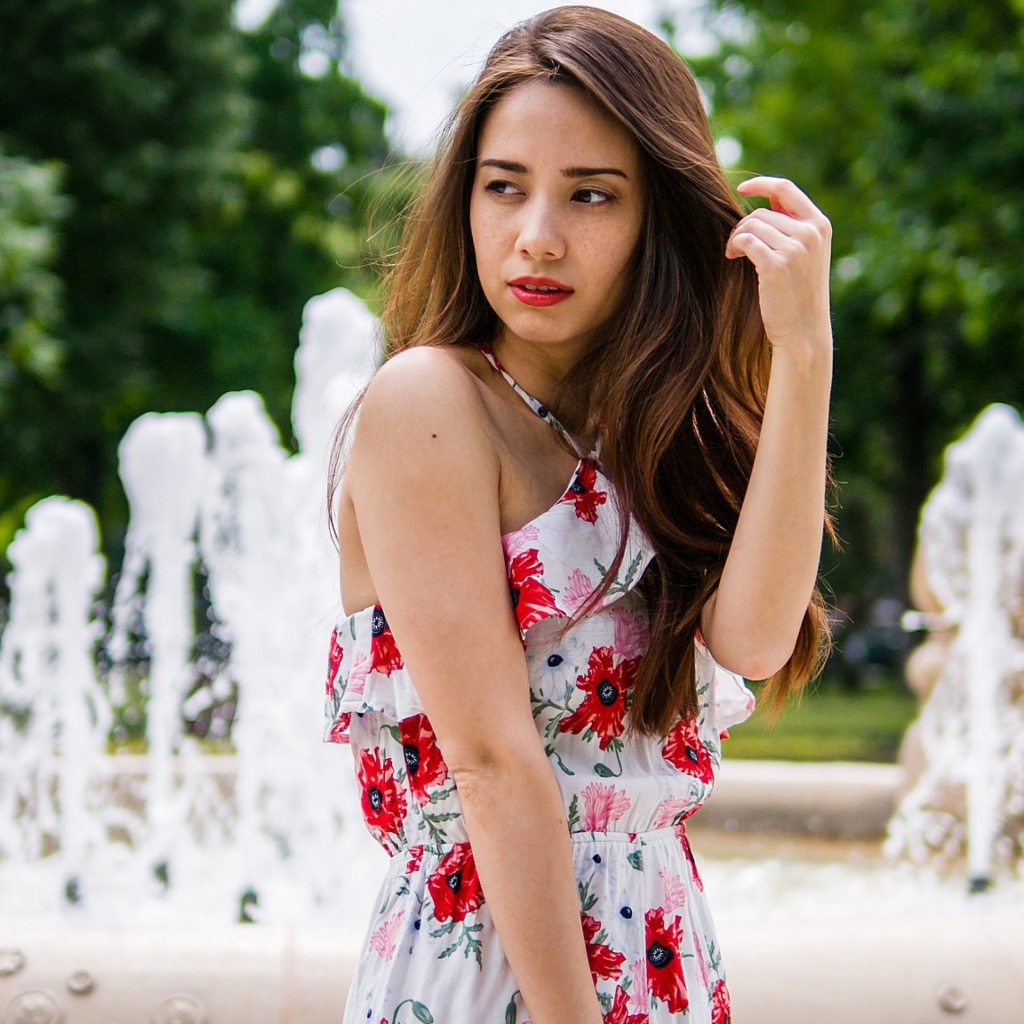 Красивая шатенка в цветастом платье у фонтана летом