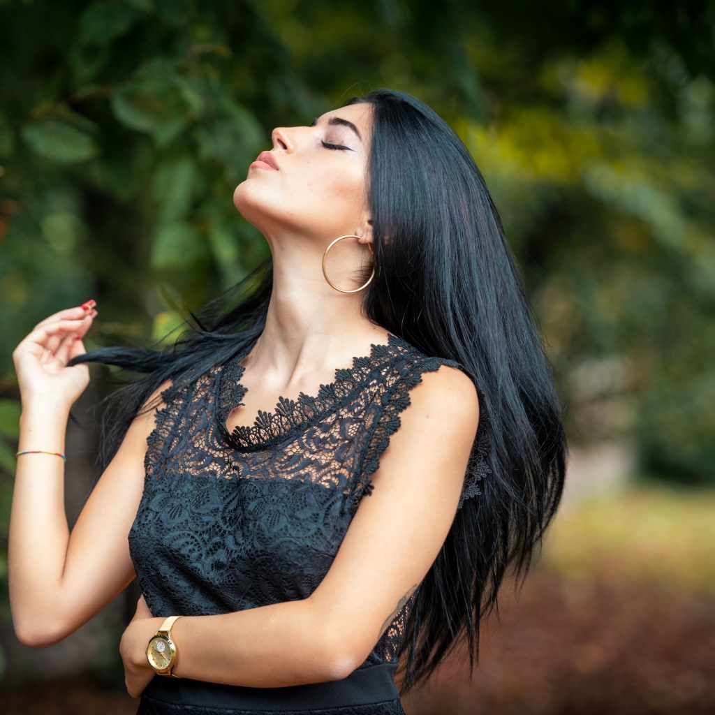 Красивая брюнетка в черном платье с закрытыми глазами в парке