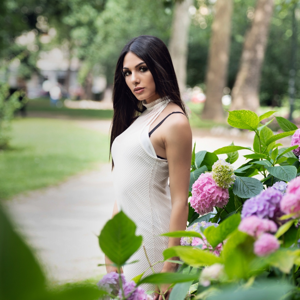 Красивая брюнетка стоит рядом с кустом гортензии