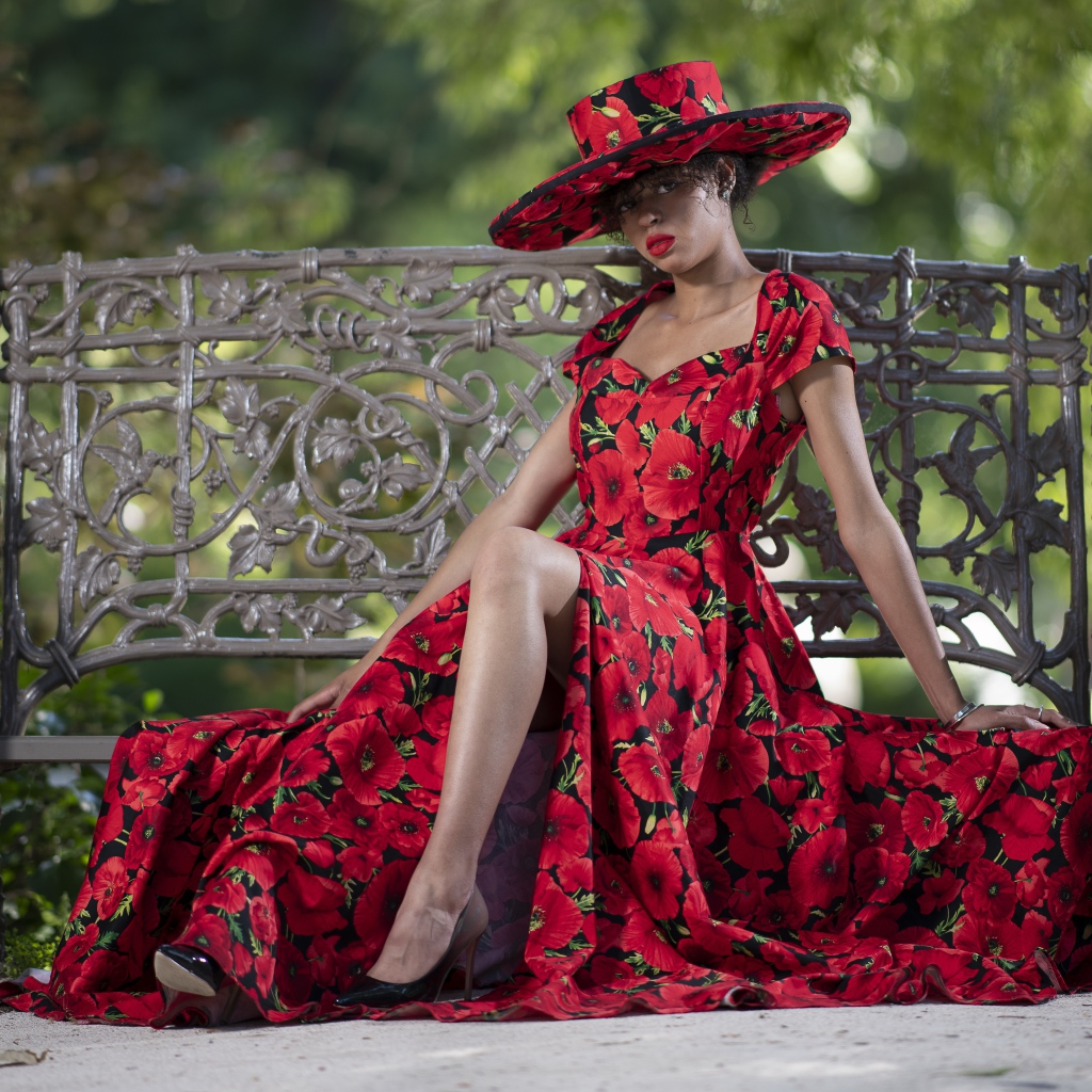 Красивая темнокожая девушка в красном платье сидит на лавке