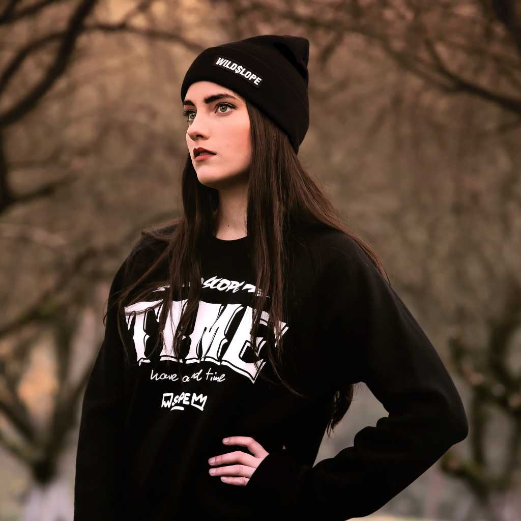 Красивая девушка в черной шапке у деревьев 