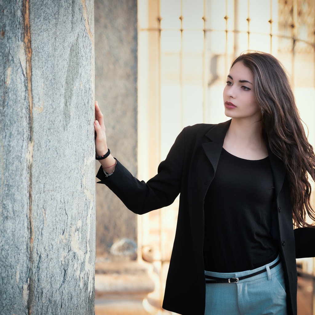 Красивая девушка в черном пиджаке стоит у стены