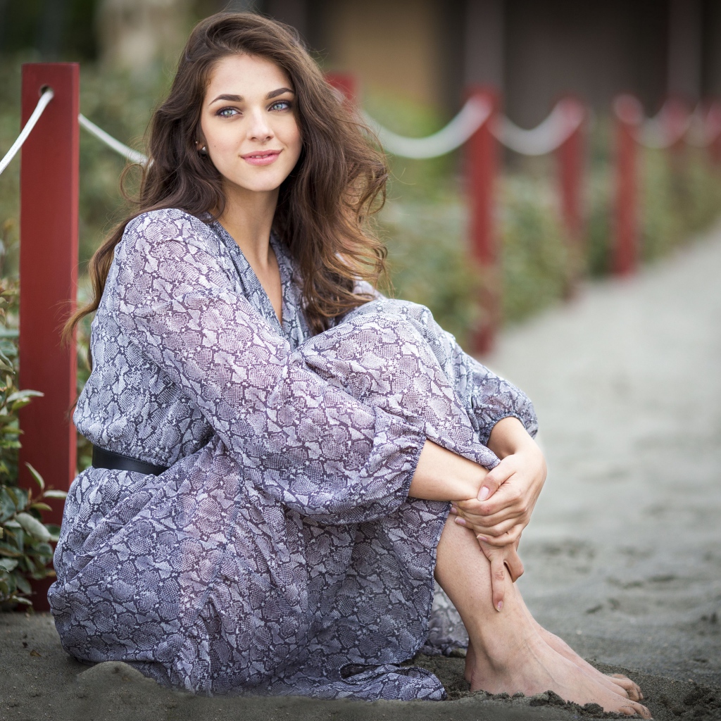 Красивая девушка в платье сидит на песке