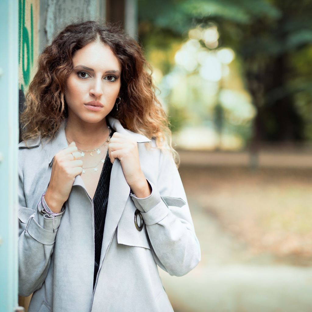 Красивая девушка в сером плаще у стены