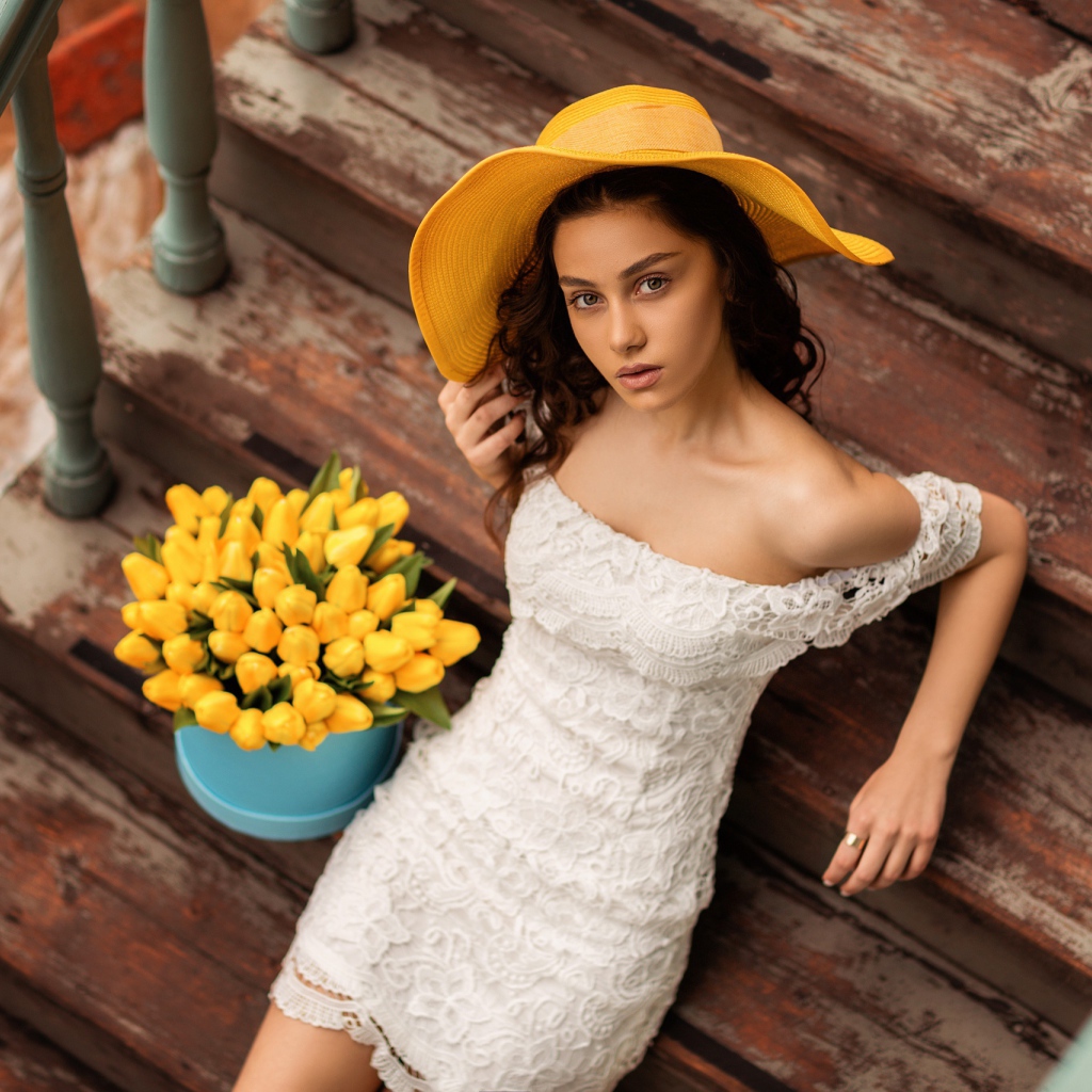 Красивая девушка в белом платье и желтой шляпе на ступеньках с букетом тюльпанов