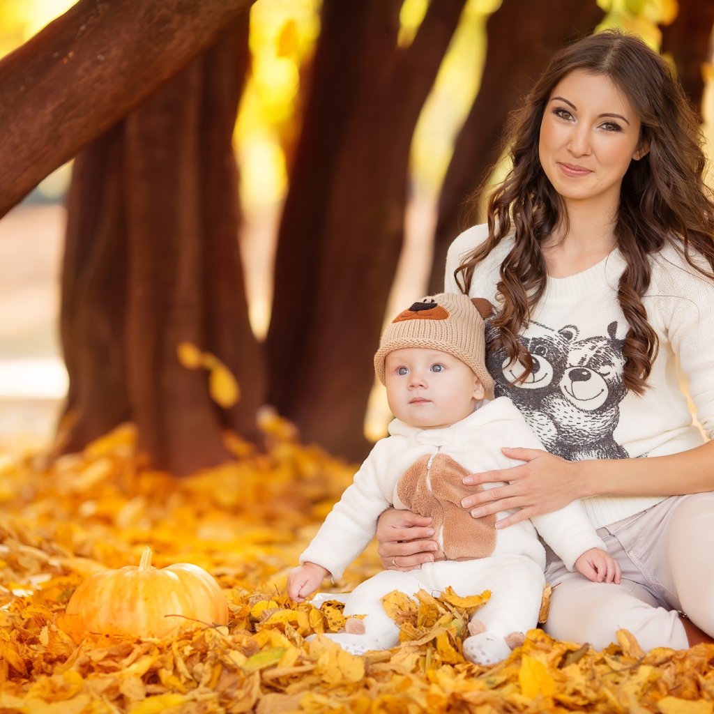 Красивая девушка сидит с грудным ребенком на опавшей листве