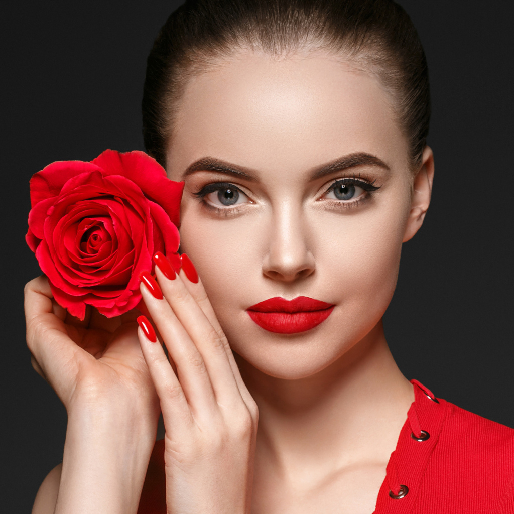 Красивая девушка с красной розой у лица на сером фоне